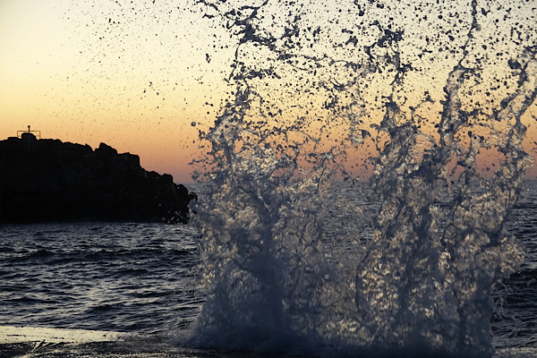 Wasser spritzt im Vordergrund hoch und wird im Dämmerlicht vom Sonnenuntergang beleuchtet